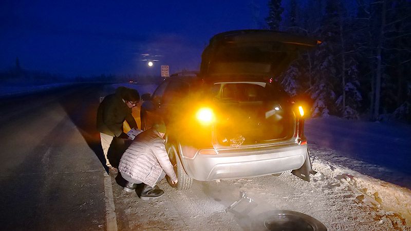アラスカの道路でタイヤを交換する地主と助けてくれる現地の人