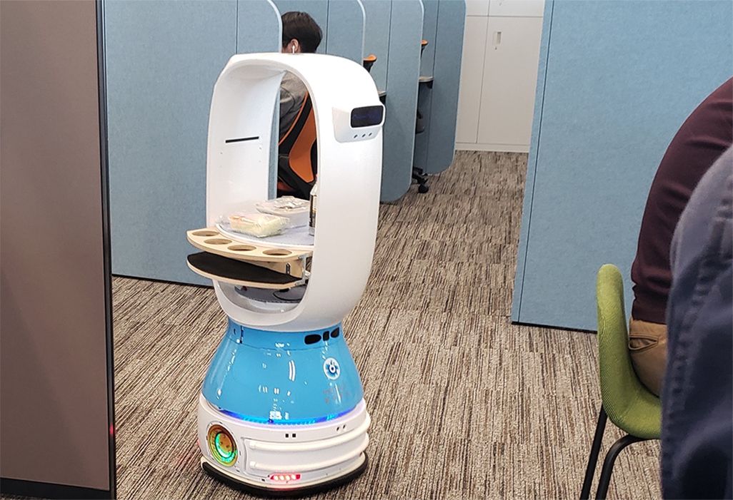 ロボットがオフィス内でデスクに飲み物を運ぶ