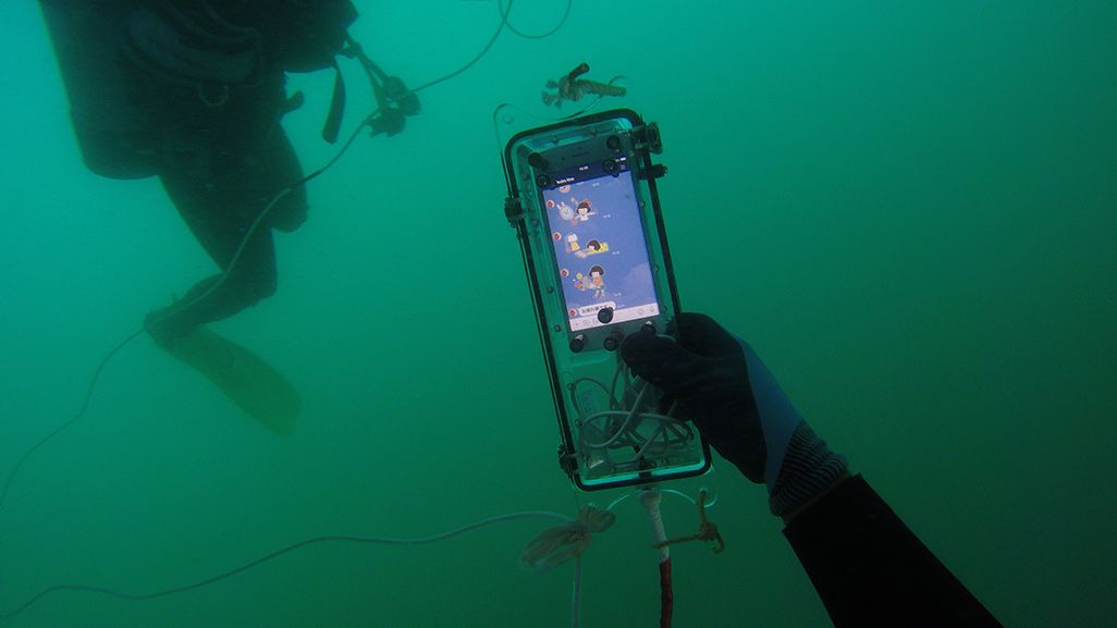 海中で防水パッケージに入ったiPhoneを手にしたダイバー