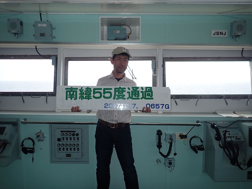 砕氷船「しらせ」の船内で「南緯55度通過」と書かれたプレートを手にする齋藤
