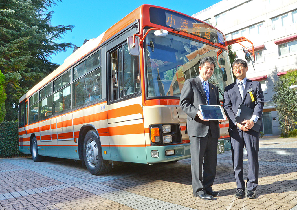 「小湊バス」の前で微笑む小湊鉄道 バス事業部の小杉直次長とKDDI株式会社 ビジネスIoT推進本部の原田圭悟