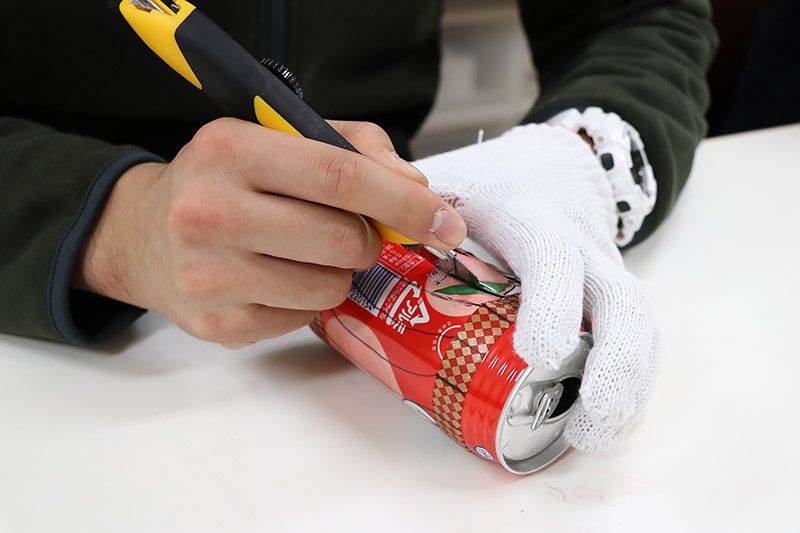空き缶にカッターの刃を入れている様子