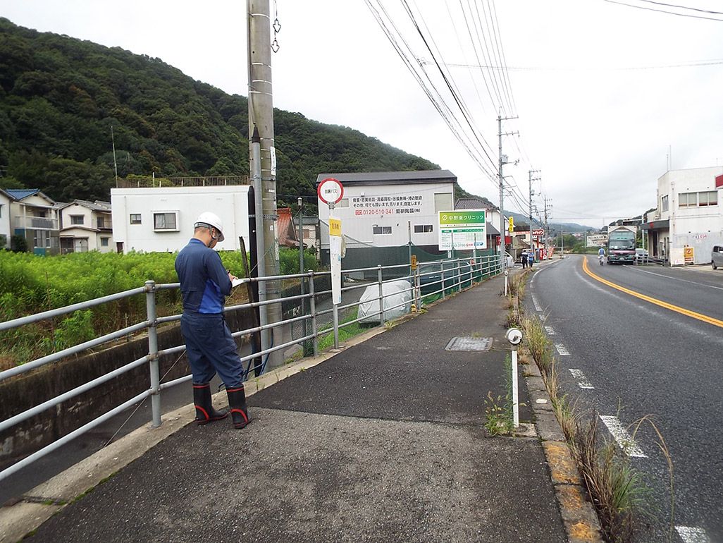 国道線沿いで光ケーブルの仮設ルートを検証する作業着姿の男性