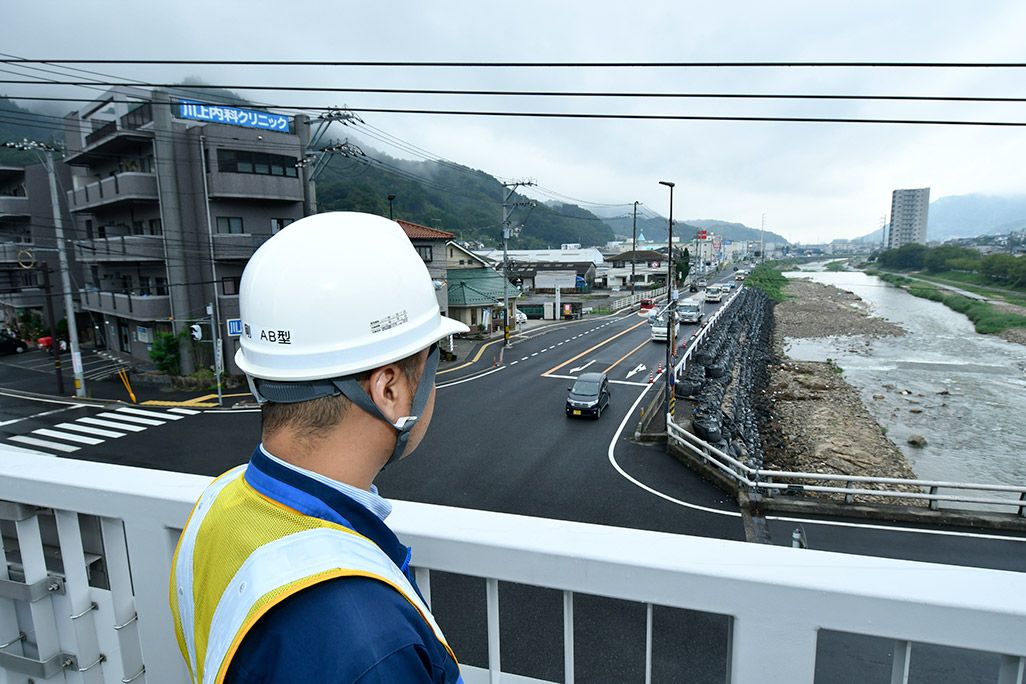 国道のと川を眺める作業着姿の男性
