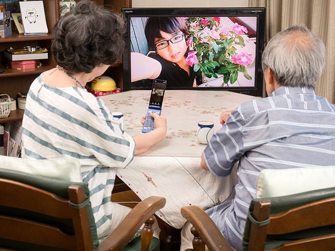 「テレビde写真」で孫の写真を眺める祖父母