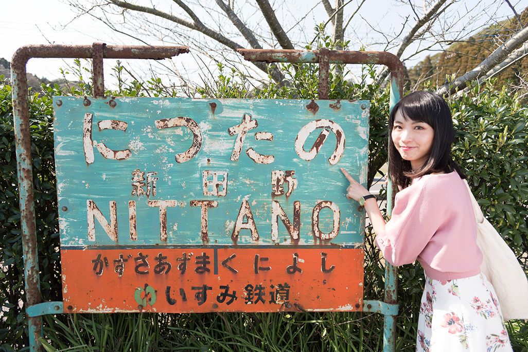 いすみ鉄道「新田野駅」の駅名標を指さす乗り鉄アイドルの伊藤桃